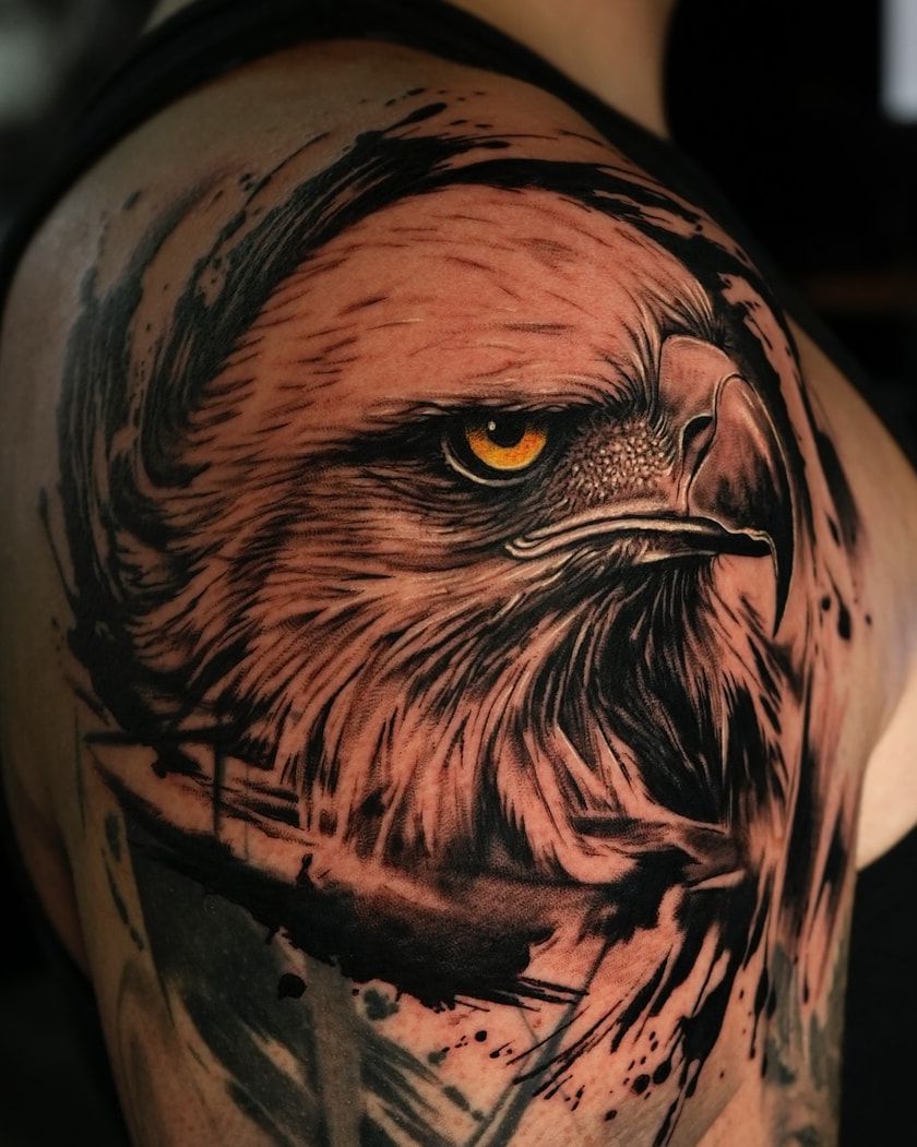 Tête d’aigle à l’œil ambré et éclaboussures d’encre, réalisme noir et gris fraîchement tatoué sur l’épaule