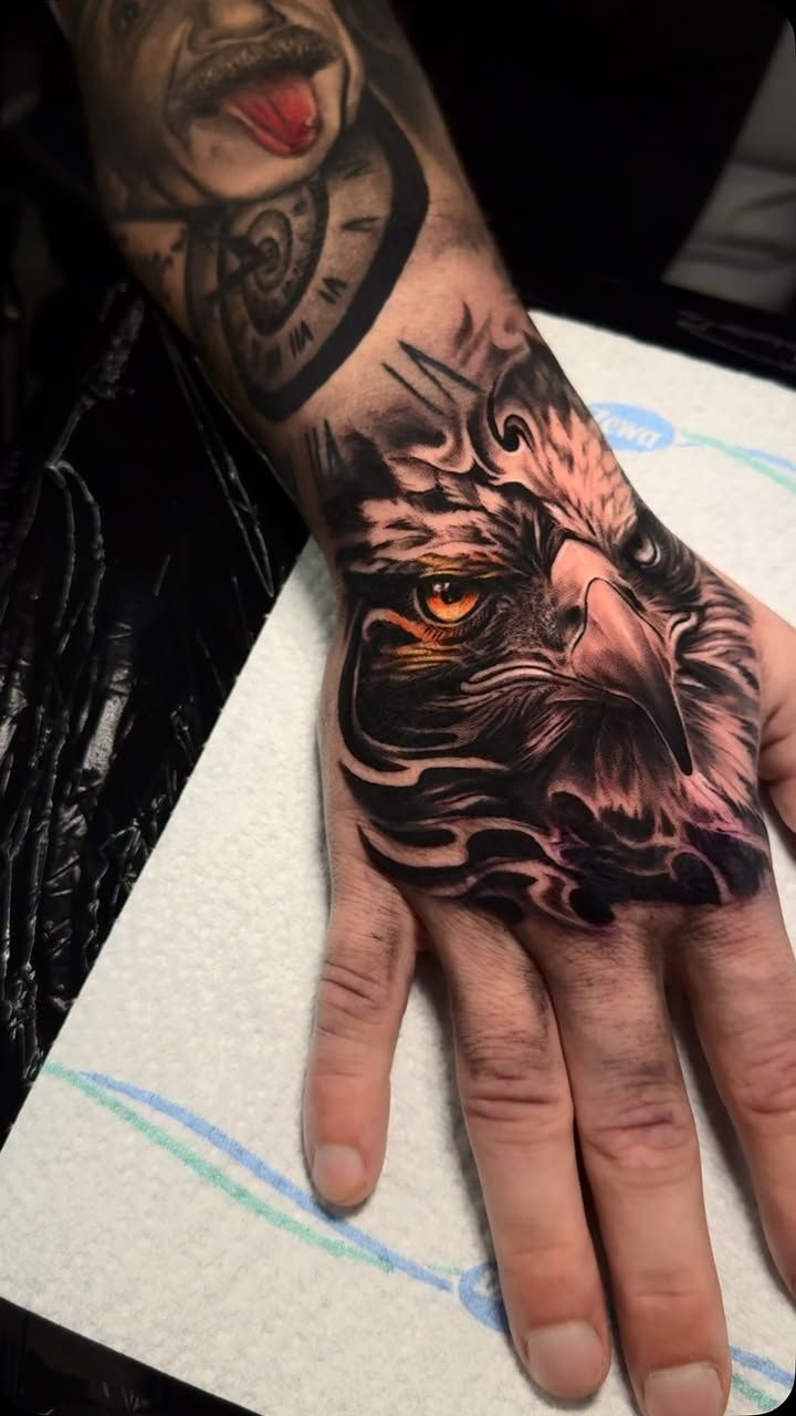 Tête d’aigle au regard ambré, plumage détaillé et volutes noires, en réalisme noir et gris couvrant le dos de la main