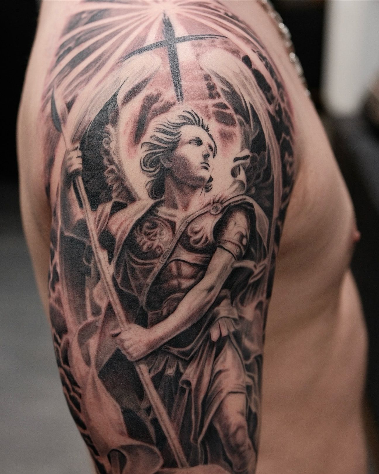 Saint Michel en armure, lance à la main sous une croix rayonnante, demi-manche en réalisme noir et gris sur l’épaule