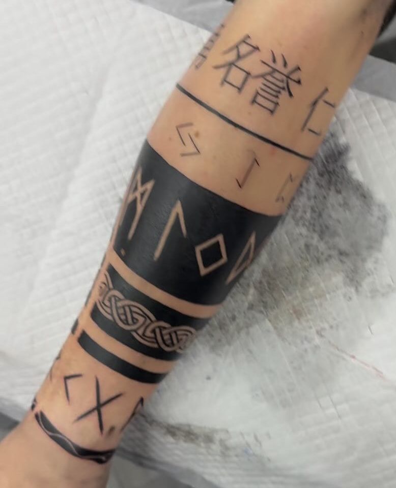 Bandes de noir plein où les runes apparaissent en peau nue, bande d’entrelacs celtique et kanji autour de l’avant-bras
