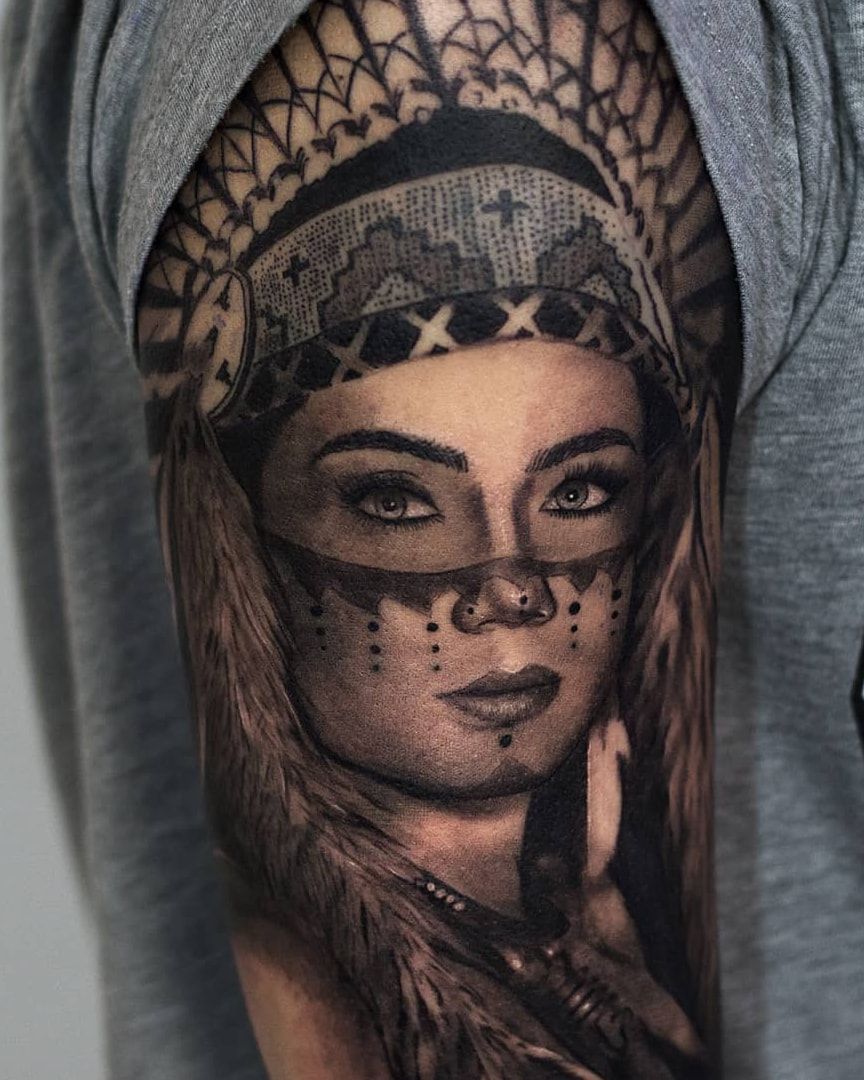 Femme amérindienne en coiffe de plumes, bande peinte sur le visage, portrait en réalisme noir et gris sur le haut du bras