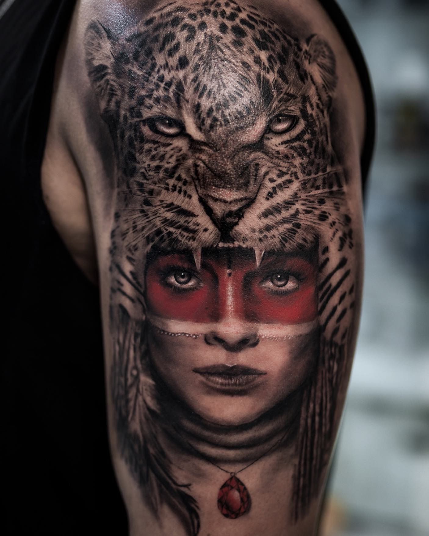 Guerrière coiffée d’une tête de jaguar, bande rouge sur les yeux et pendentif rouge, réalisme noir et gris sur l’épaule