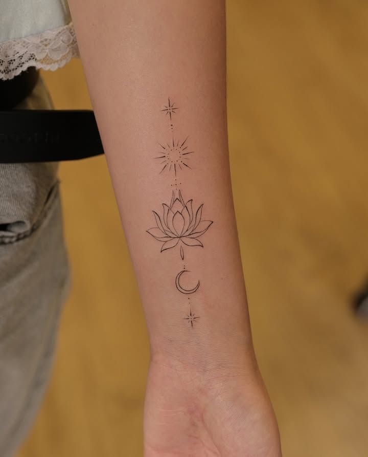 Fleur de lotus encadrée d’un soleil, d’un croissant de lune et de deux étoiles, alignés en fine line minimaliste sur l’intérieur de l’avant-bras