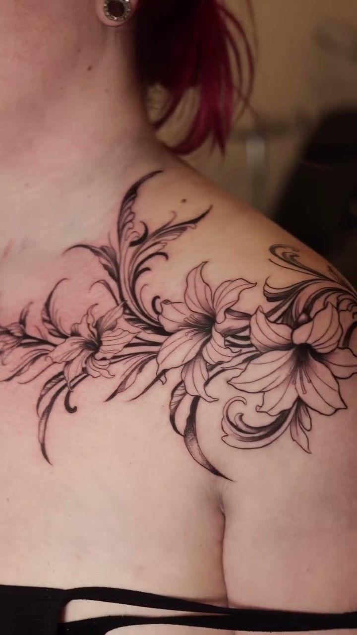 Lys et volutes noires effilées le long de la clavicule jusque sur l’épaule, ornement floral en noir et gris