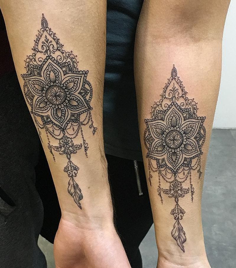 Deux mandalas assortis aux pendentifs de perles et de plumes, au trait fin et en pointillé, sur l’intérieur de deux avant-bras