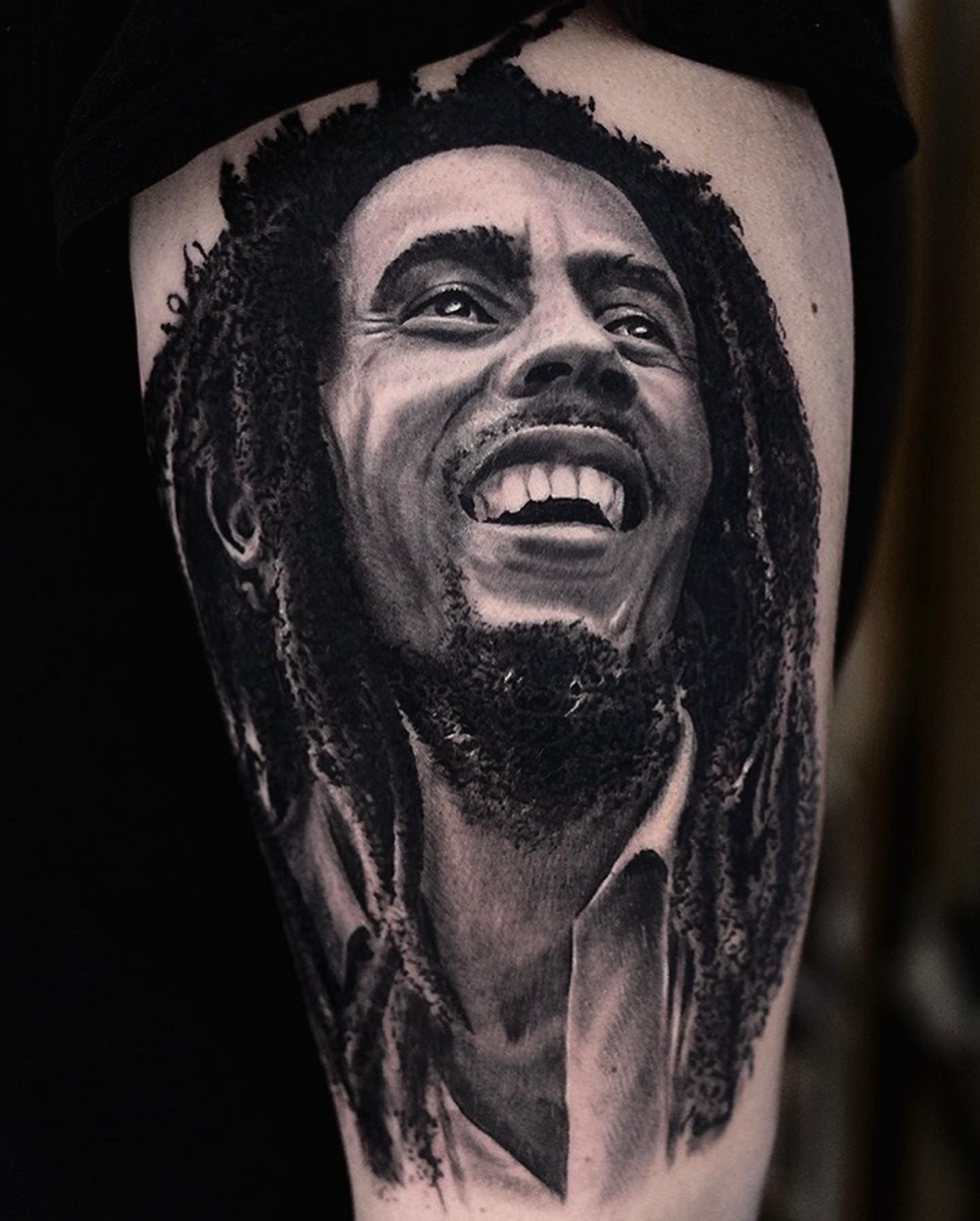 Bob Marley en plein éclat de rire, dreadlocks et barbe aux noirs denses, portrait réaliste noir et gris sur la cuisse