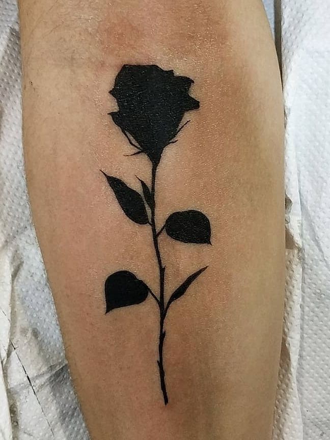 Silhouette de rose en noir plein sur l’avant-bras, réalisée pour recouvrir un petit lettrage