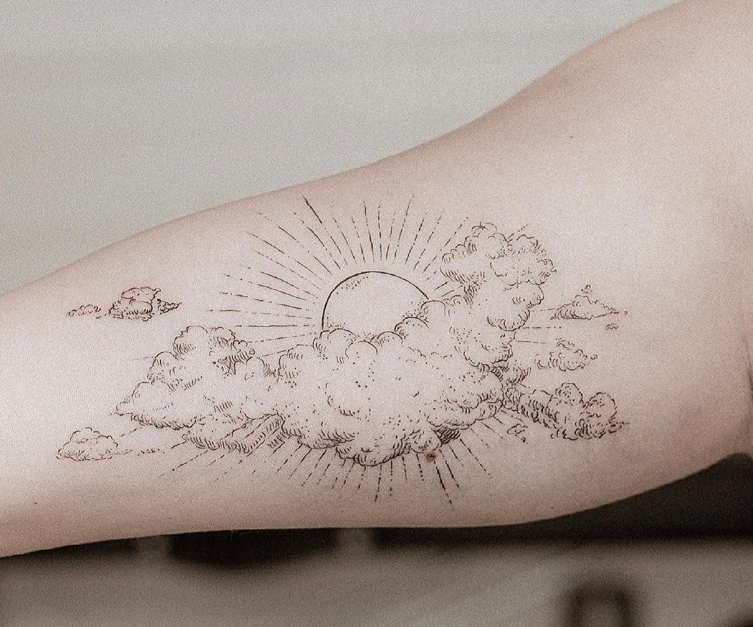 Soleil rayonnant derrière des nuages dessinés en hachures façon gravure, au trait fin sur l’intérieur du bras