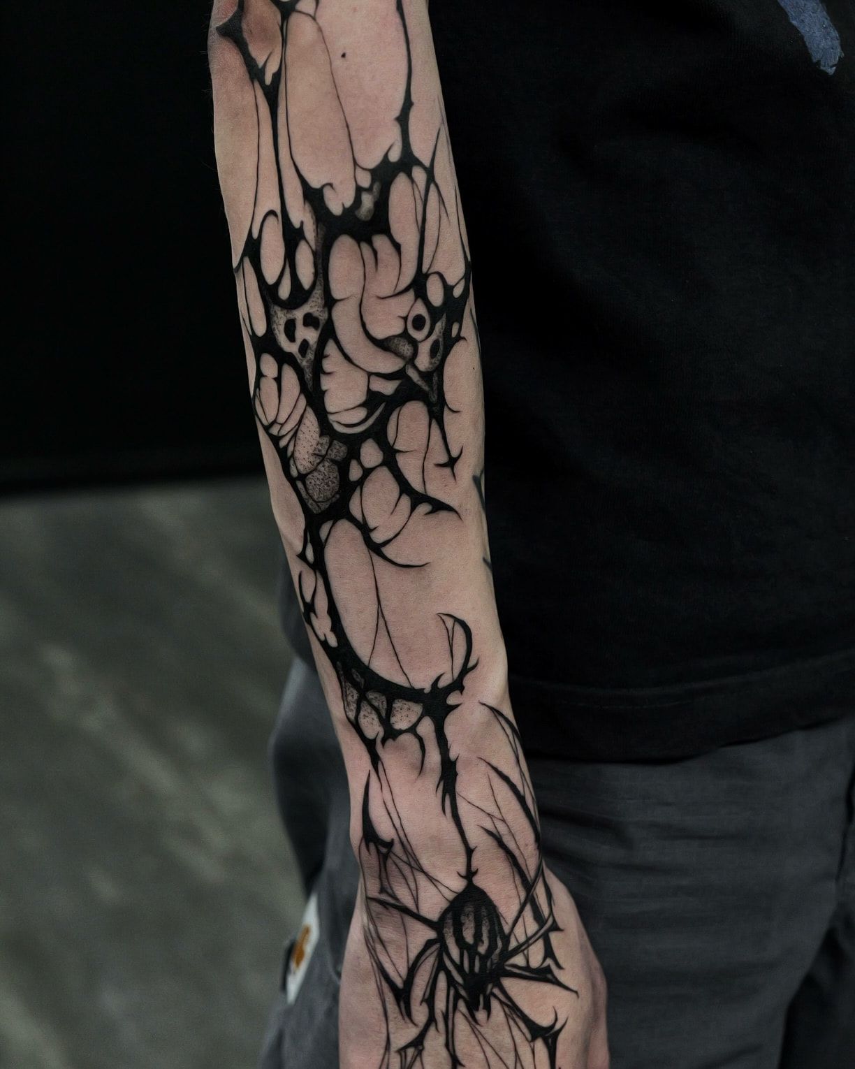 Blackwork aux formes organiques et épineuses le long de l’avant-bras, jusqu’à une araignée sur le dos de la main