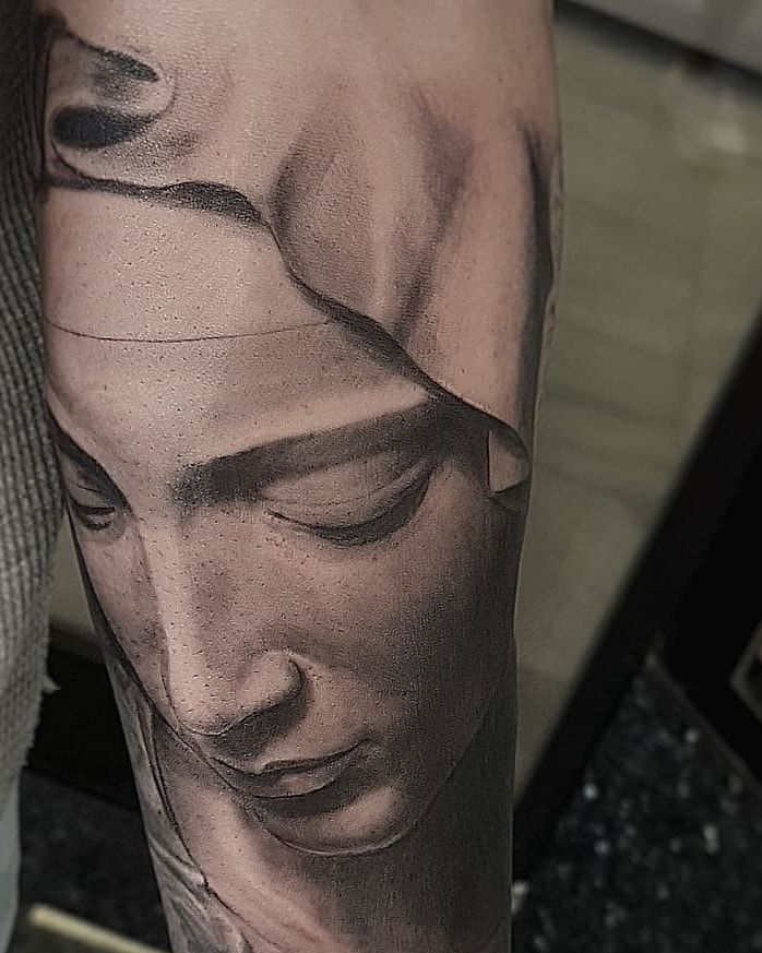 Visage voilé de la Vierge de la Pietà de Michel-Ange, paupières baissées, réalisme noir et gris sur l’avant-bras