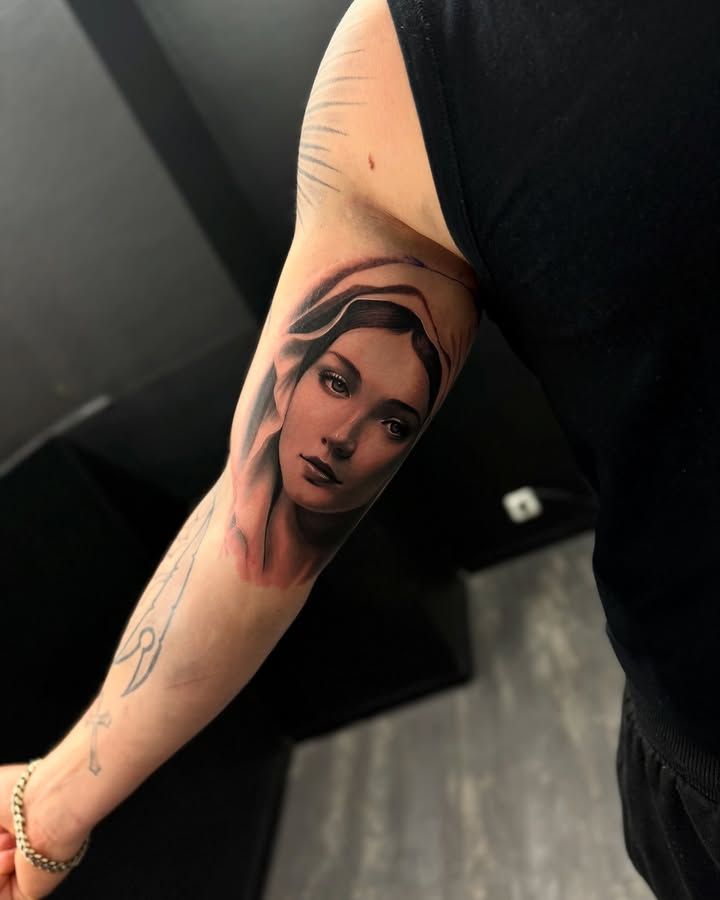 Visage de la Vierge enveloppé d’un voile, au regard doux, en réalisme noir et gris fraîchement tatoué à l’intérieur du haut du bras