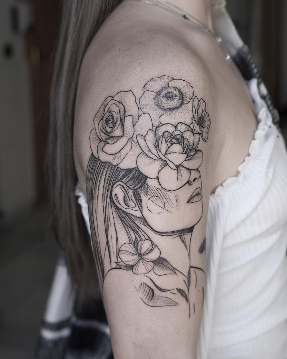 Visage de femme aux yeux cachés sous des roses et des pavots, fine line et ombrages en pointillé sur le haut du bras